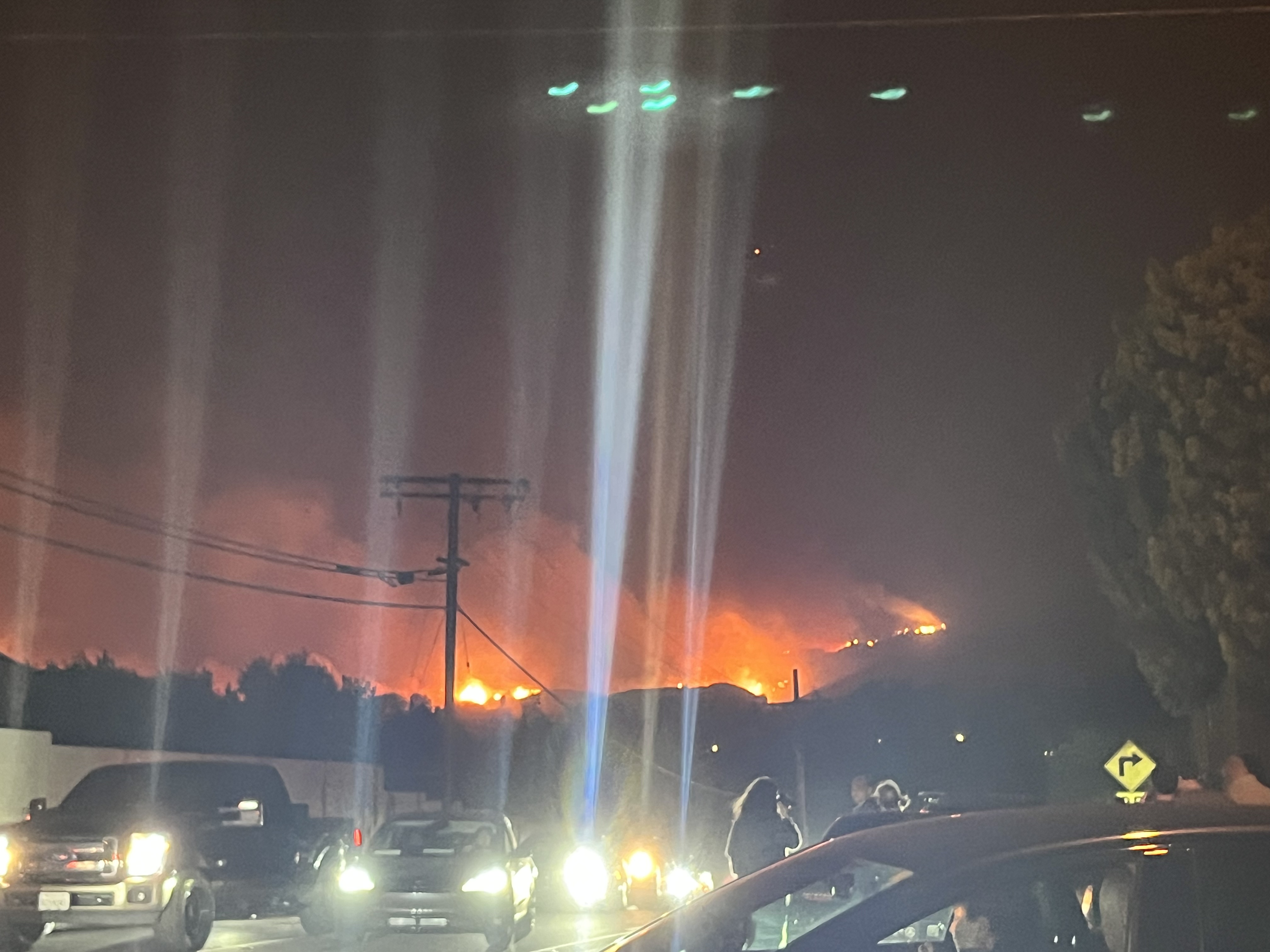 cars driving in the night escaping flames in the hills beyond
